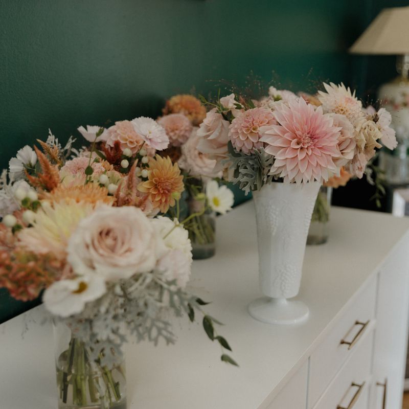 Bridal and bridesmaid bouquets in blush, peach and cream lined up on a white dresser against a deep green wall at The Fitzgerald in Milwaukee